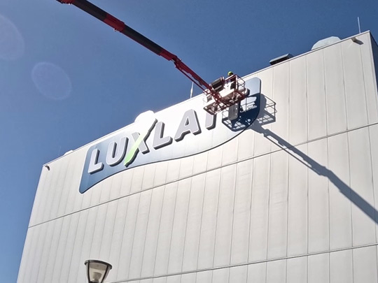 Enseigne lumineuse sur panneau de fond placée en haut du bâtiment vertigineux de Luxlait.